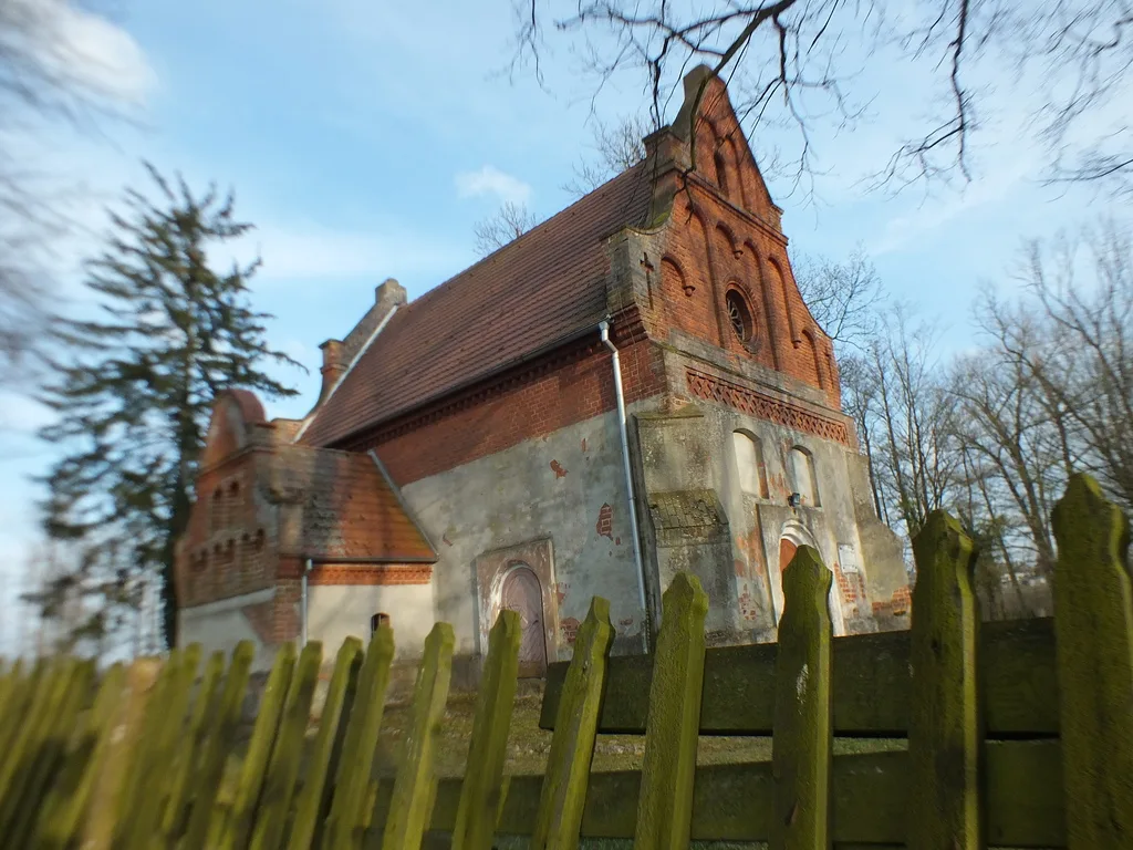 Stary kościół z czerwonej cegły sfotografowany zza drewnianego płotu.