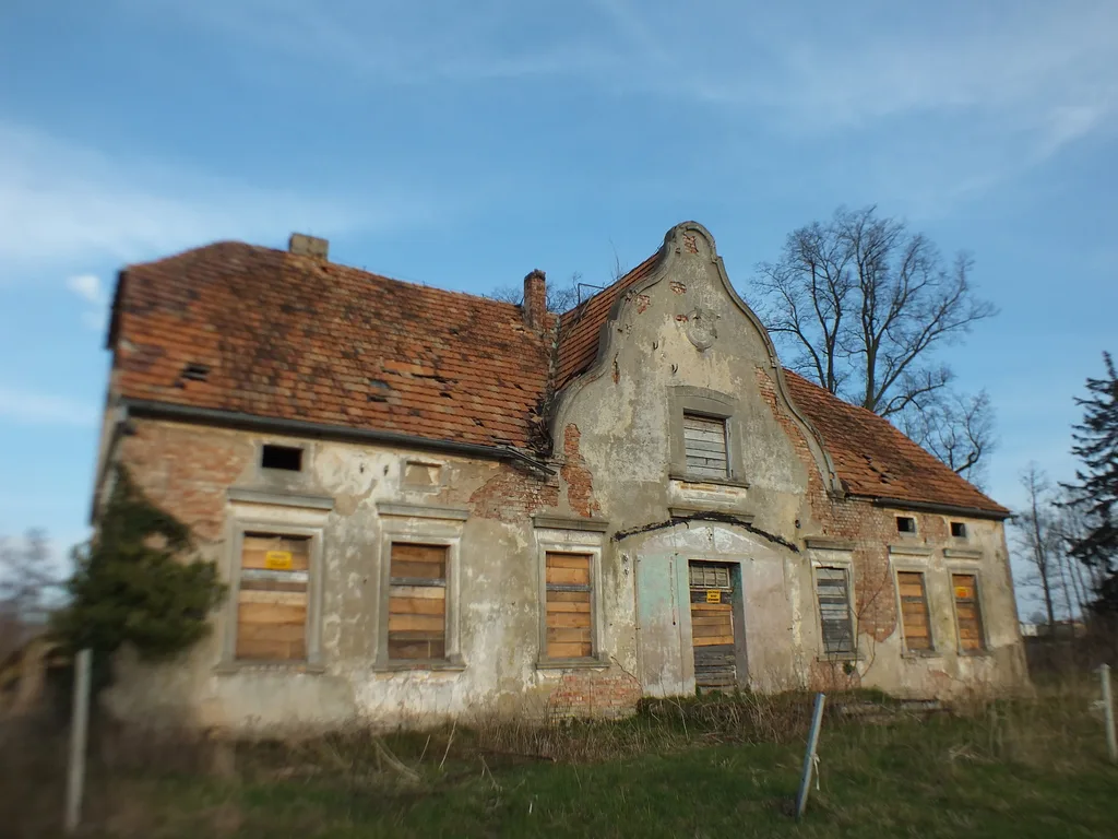Mocno zniszczony budynek niewielkiego dworku.