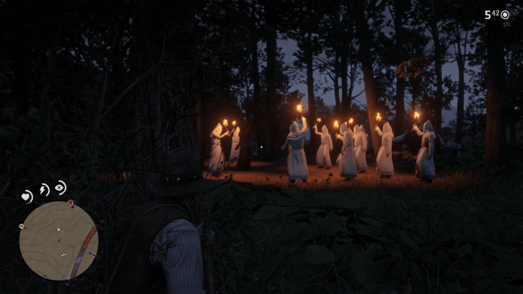 Przyczajony Arthur Morgan obserwuje z krzaków nocne spotkanie Ku Klux Klanu: grupa osób w białych szatach trzyma w rękach zapalone pochodnie.