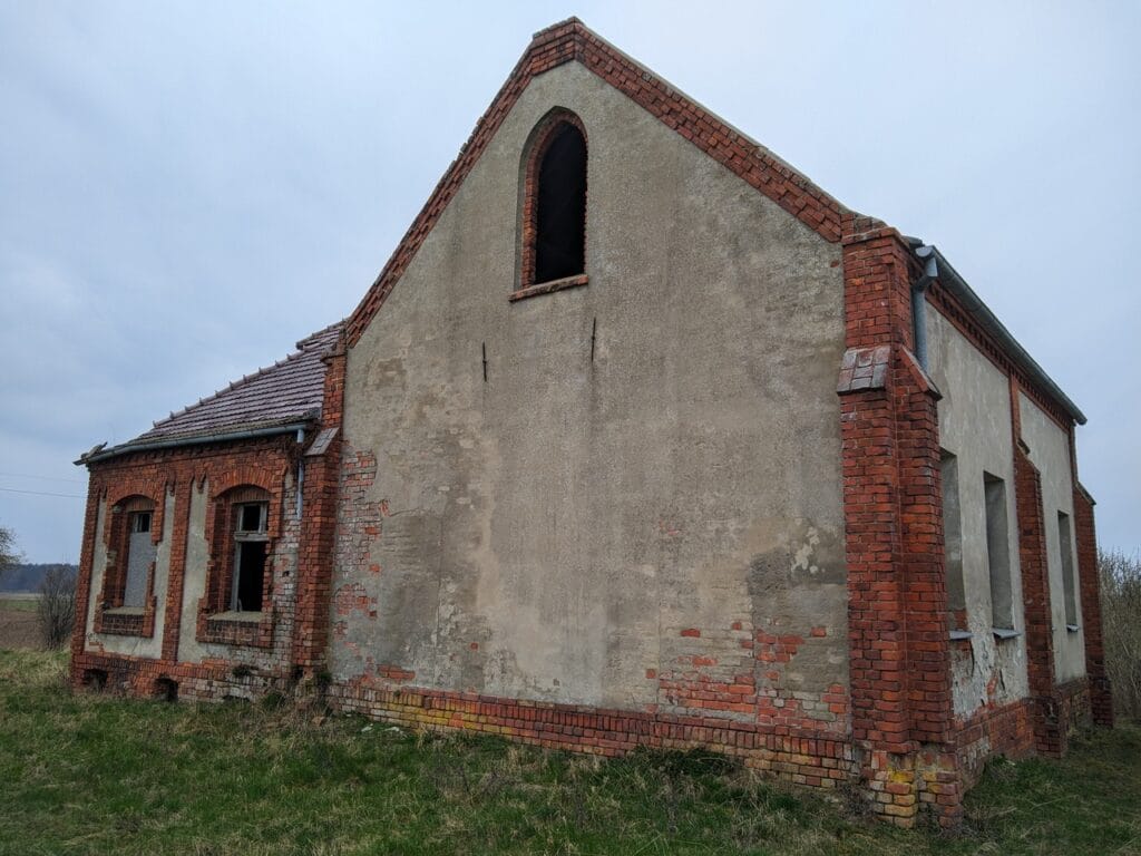 Tył sali modlitewnej. Pełna ściana z oknem zwieńczonym ostrym łukiem w górnej częsci budynku.