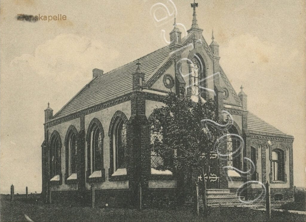 Stare zdjęcie w kolorach sepii, przedstawiające kaplicę w oryginalnym stanie. Widoczny front budynku z głównym wejściem i lewa ściana z rzędem czterech ostrołukowych okien. Przed budynkiem nieduże drzewo.