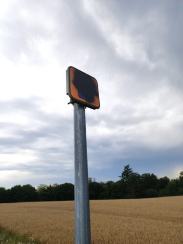 Na słupku jest oznaczenia Starego Szlaku Kolejowego (pomarańczowy kwadrat, czarny symbol roweru, biała liczba 15 na niebieskim polu) zamalowane czarną farbą.