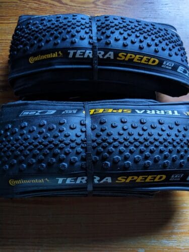 Dwie zwinięte opony leżą na drewnianym stole. Na bocznych ściankach mają żółte i białe napisy Continental Terra Speed.