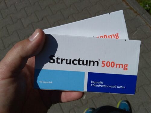 Dłoń trzymająca dwa opakowania leku Structum. 60 kapsułek po 500 mg chondroitini natrii sulfas. 