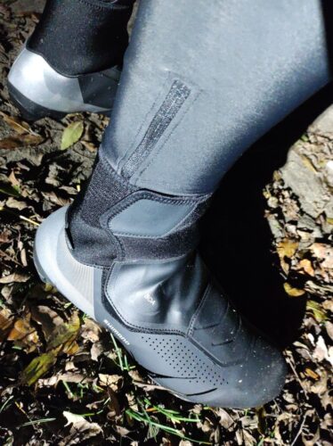 Noc. W świetle mocnego światła rowerowego prezentuję prawą stopę w nowym bucie, z czubkiem lekko pochlapanym błotem. W tle widać część lewej stopy. Pięty na butach pokryte są czymś srebrzystym, nie do końca odblaskowym, ale i tak dobrze widocznym w świetle lampy.