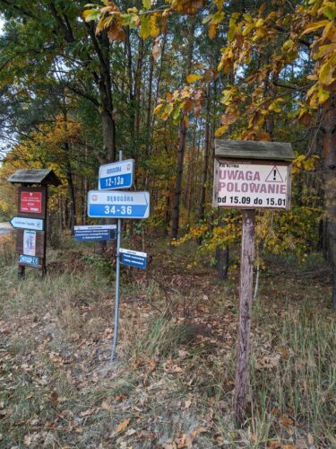 Na skraju lasu stoi szereg znaków. Po prawej stronie jest tablica Nadleśnictwu Szubin, Leśnictwo Tupadły a pod nią drogowskaz do leśnictwa. W środku drogowskazy do domów w miejscowości Dębogóra oraz do pozostałości cmentarza ewangelickiego. Z prawej jest tablica PZŁ Kcynia ze znakiem ostrzegawczym, napisem „Uwaga polowanie” i dopiskiem „od 15.09 do 15.01”