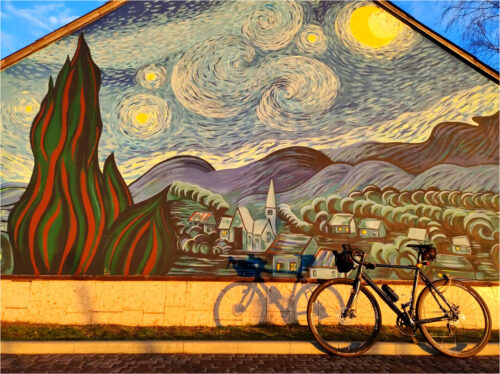 Rower oparty przed ścianą budynku z muralem – repliką obrazu „Gwieździsta noc” Vincenta van Gogha.