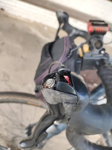 Zbliżenie na lewą klamkomanetkę. Jest pobrudzona i porysowana, a plastikowa kopułka osłaniająca wskaźnik przełożenia została odłamana i zostały jej tylko resztki.