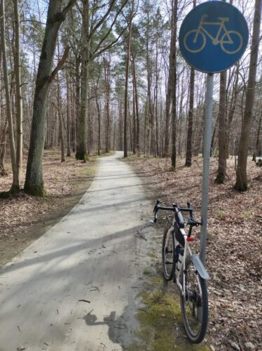 O stojący przy leśnej drodze dla rowerów znak C-13 (biały symbol roweru na okrągłym niebieskim polu) opiera się moja szutrówka.
