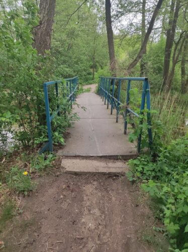 Wąski betonowy mostek z niebieskimi barierkami.