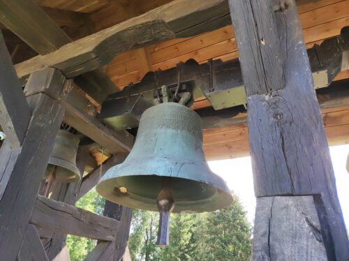 Zbliżenie na wiszący w drewnianej dzwonnicy spory dzwon, na którym widać napis "In memoriam anno 1817"