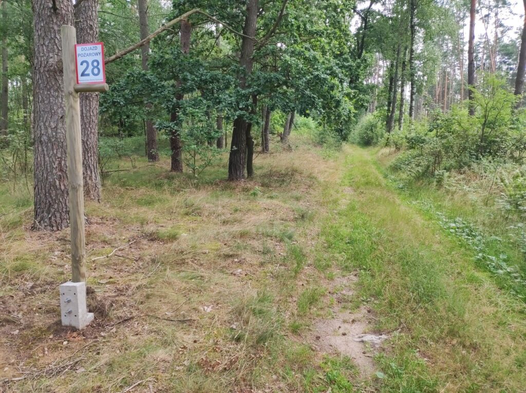Tym razem droga jest głównie trawiasta. Po prawej stoi drewniany słupek z tabliczką „Dojazd pożarowy 28”